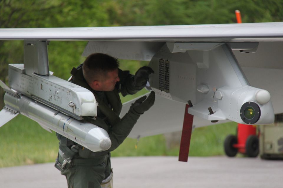 Pilot working on a pylon on an F-16 on the ground.